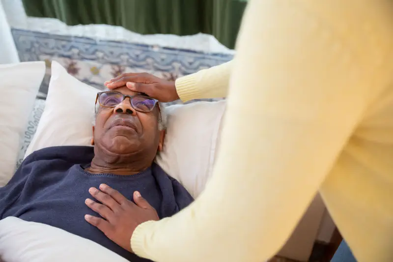A caregiver gently checks on an older man resting in bed