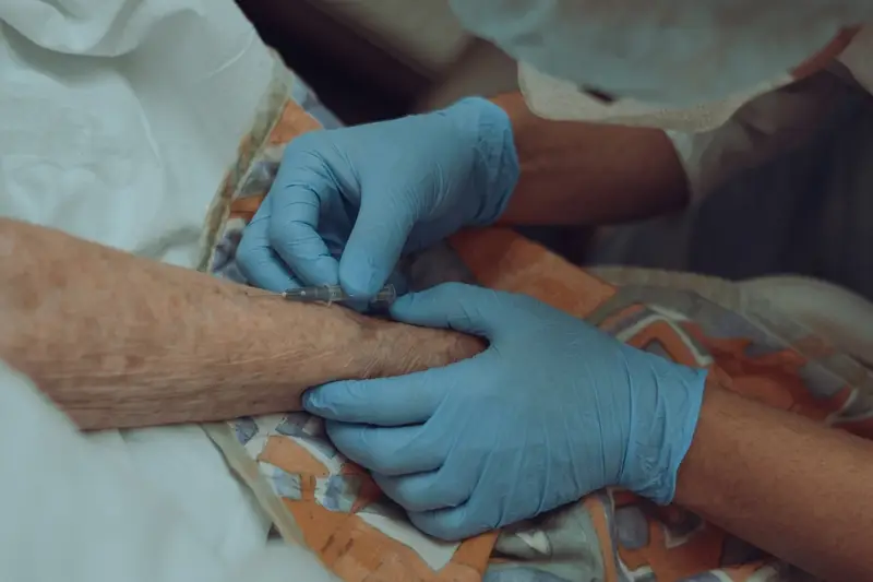 A nurse in gloves gently starts an IV in an older patient's arm